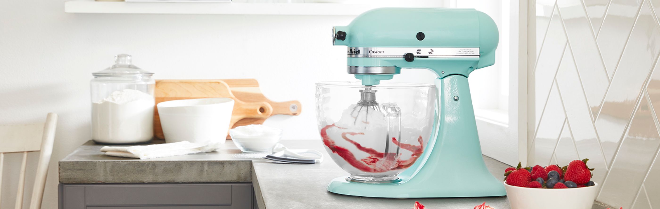 A teal KitchenAid® stand mixer with a bowl of mixed berries.