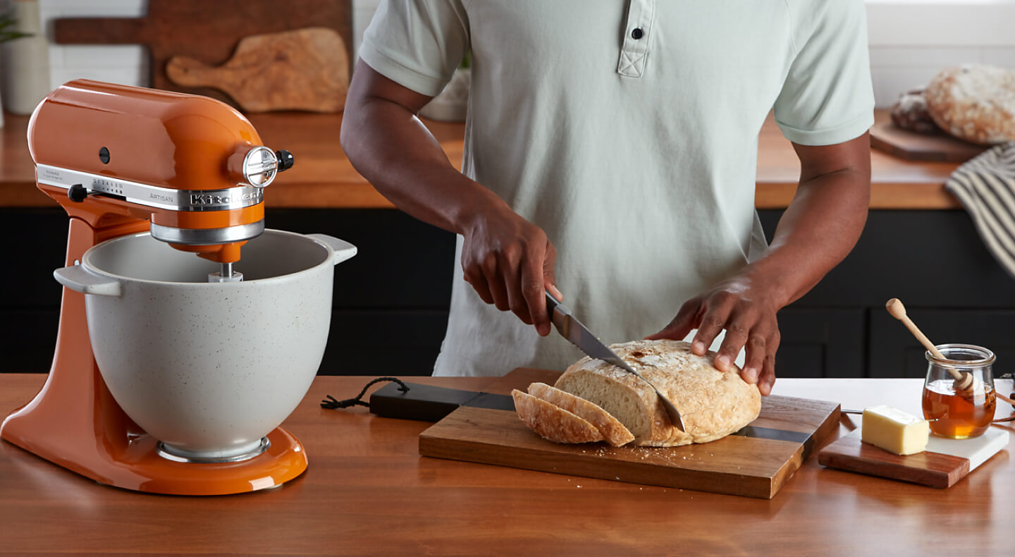 Person slicing freshly baked bread next to a KitchenAid® stand mixer