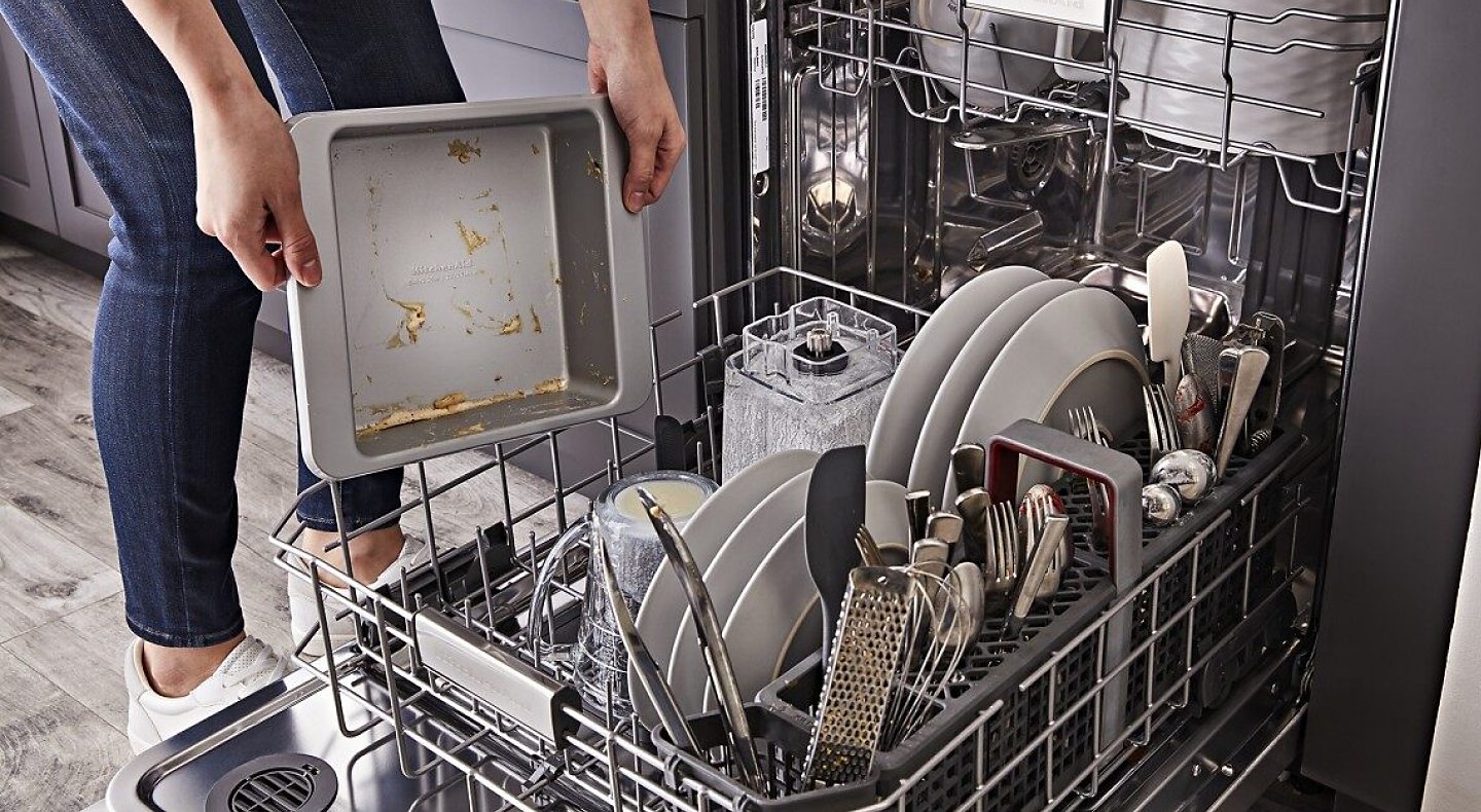 A person loading a dirty pan into the bottom rack of a KitchenAid® dishwasher
