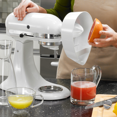 A person using the Citrus Juicer Attachment on a white KitchenAid® stand mixer