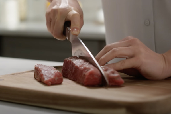 Person cutting meat with knife on a wood cutting board