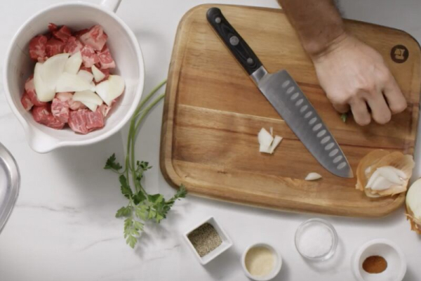 Person cutting onion to put into bowl with meat