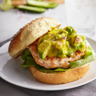 Salmon burger topped with avocado on white plate