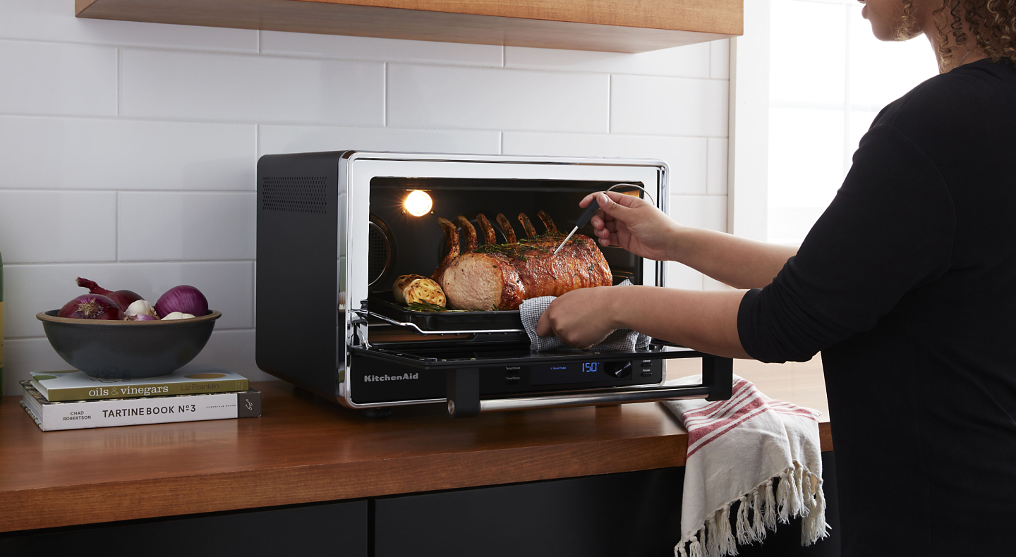 A pork roast being removed from a KitchenAid® Countertop Oven