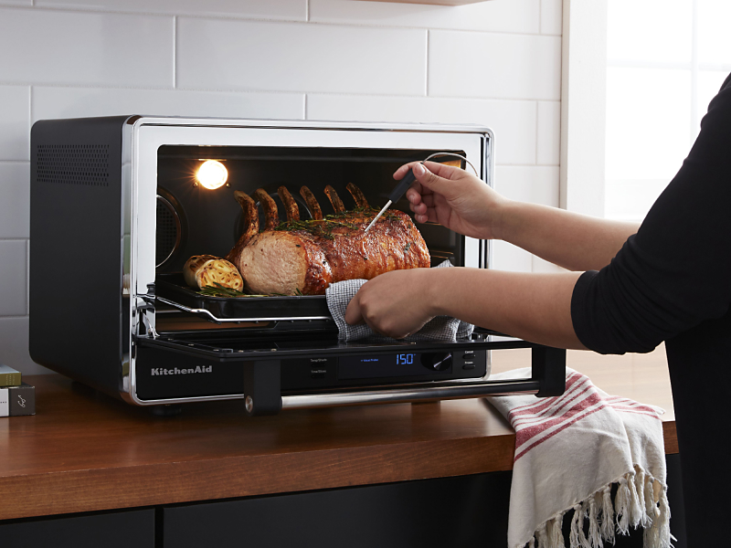 A pork roast being removed from a KitchenAid® Countertop Oven