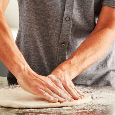 Close-up of Maker hands flattening a round of pizza dough