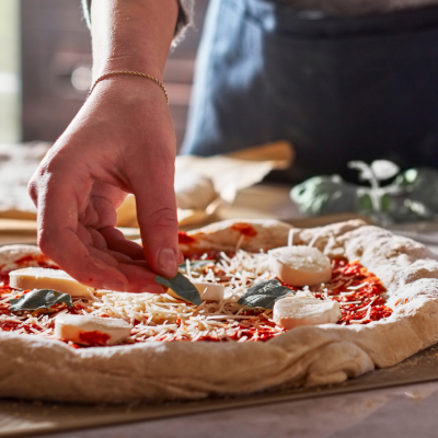 Maker adding ingredients to top of pizza