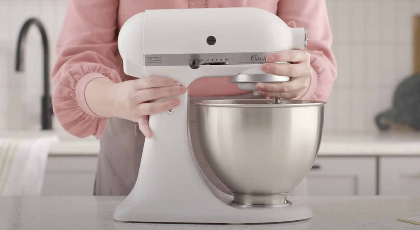 Person holding white, KitchenAid® stand mixer with stainless steel bowl