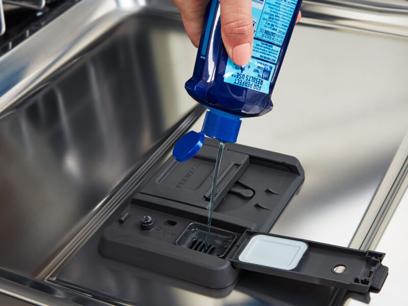 Close-up of person adding rinse aid to dishwasher rinse aid compartment