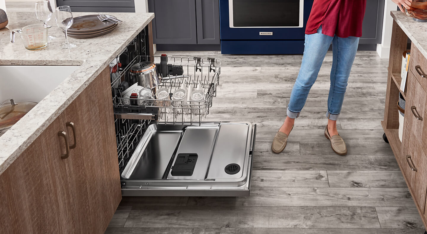 Person standing next to partially loaded dishwasher with top rack extended