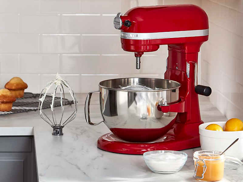 KitchenAid® stand mixer next to a wire whip accessory with stiff egg white peaks and frosted muffins in modern kitchen.