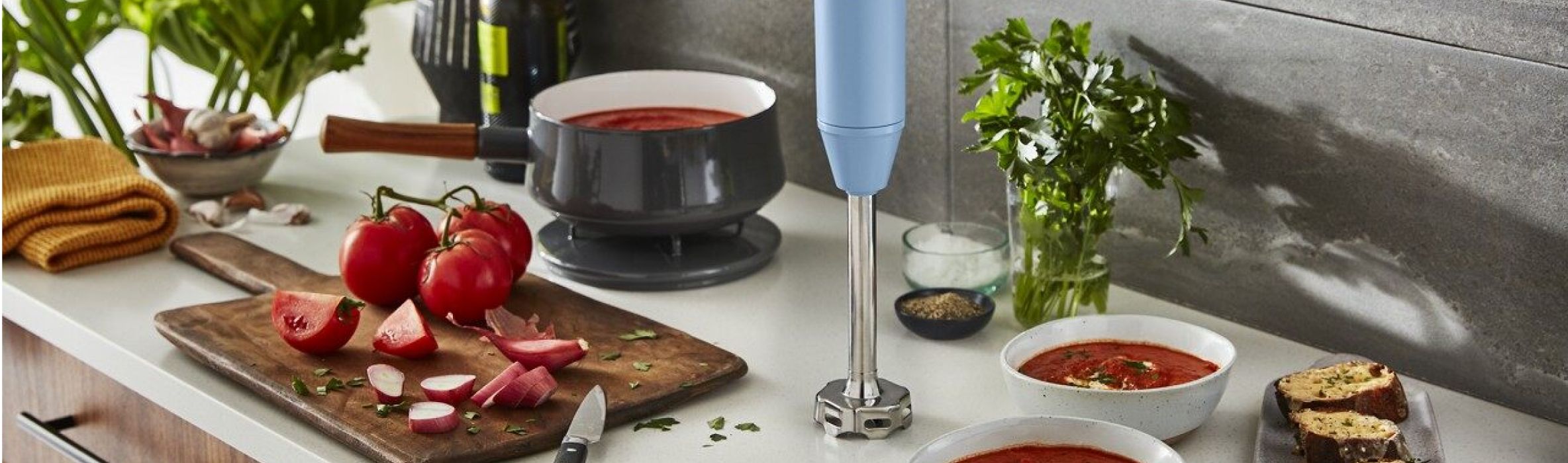 Ingredients for making marinara sauce on a countertop beside a KitchenAid® hand blender.