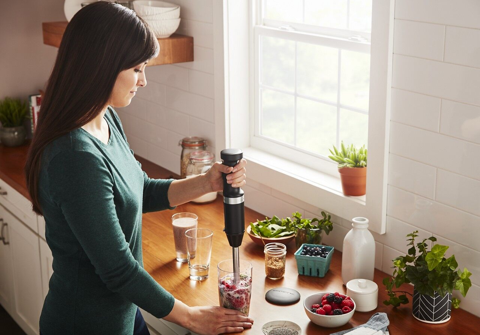A woman making a smoothie with a KitchenAid® hand blender.