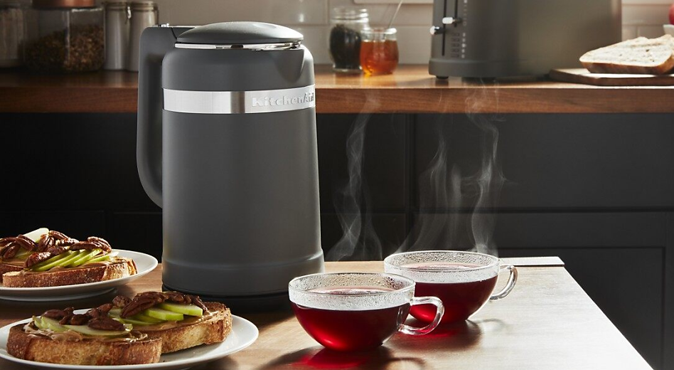 Electric tea kettle on a kitchen island next to cups of tea and toast.