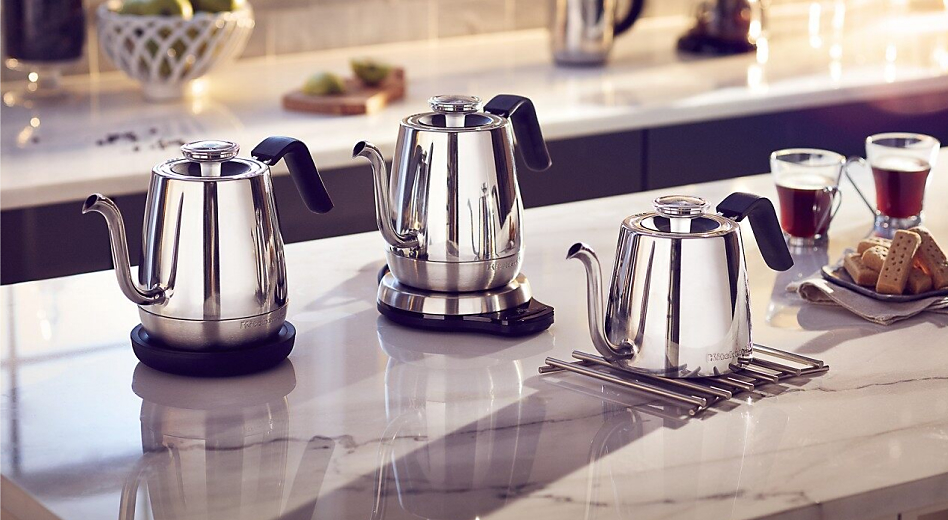 Three KitchenAid® electric tea kettles on the island next to cups of tea and cookie tray.