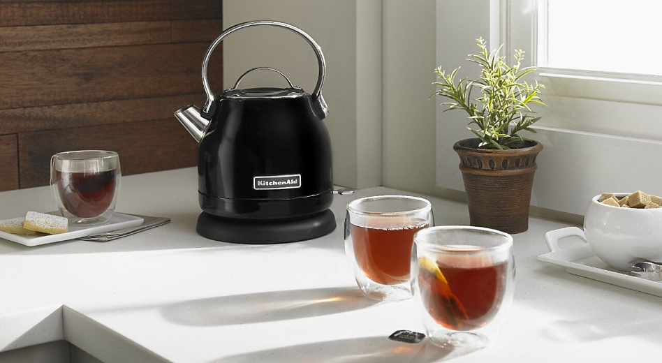 Black KitchenAid® 1.25 L Electric Kettle on a counter next to full cups of tea.
