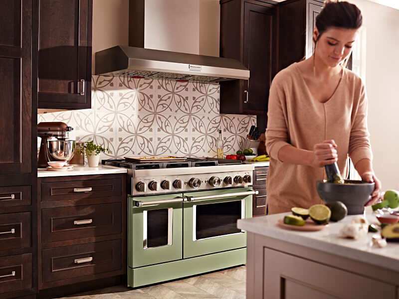 KitchenAid® range set in cabinetry behind person preparing food at an island