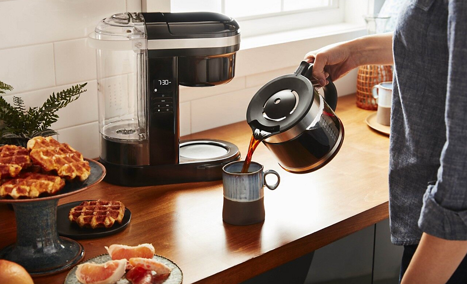 Woman pouring coffee into a mug with coffee maker in background
