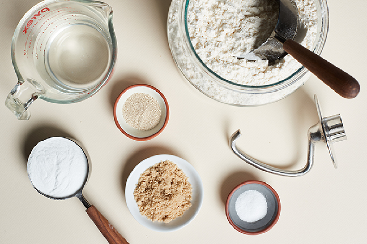 Dough ingredients and measuring cups next to a dough hook