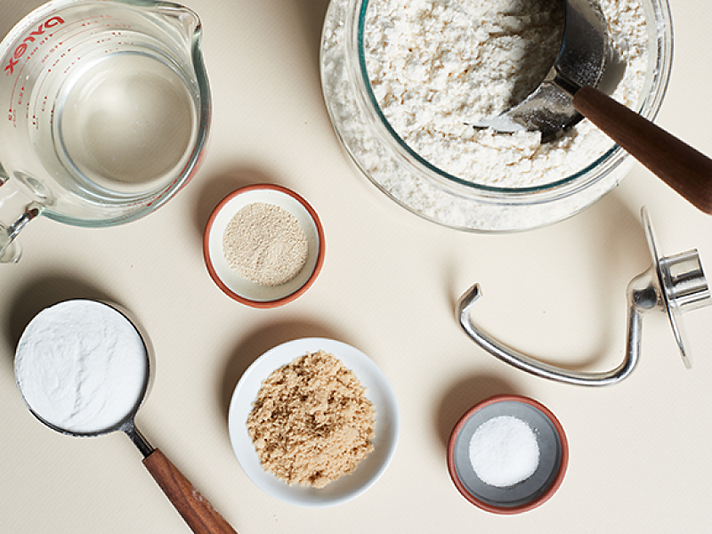Dough ingredients and measuring cups next to a dough hook