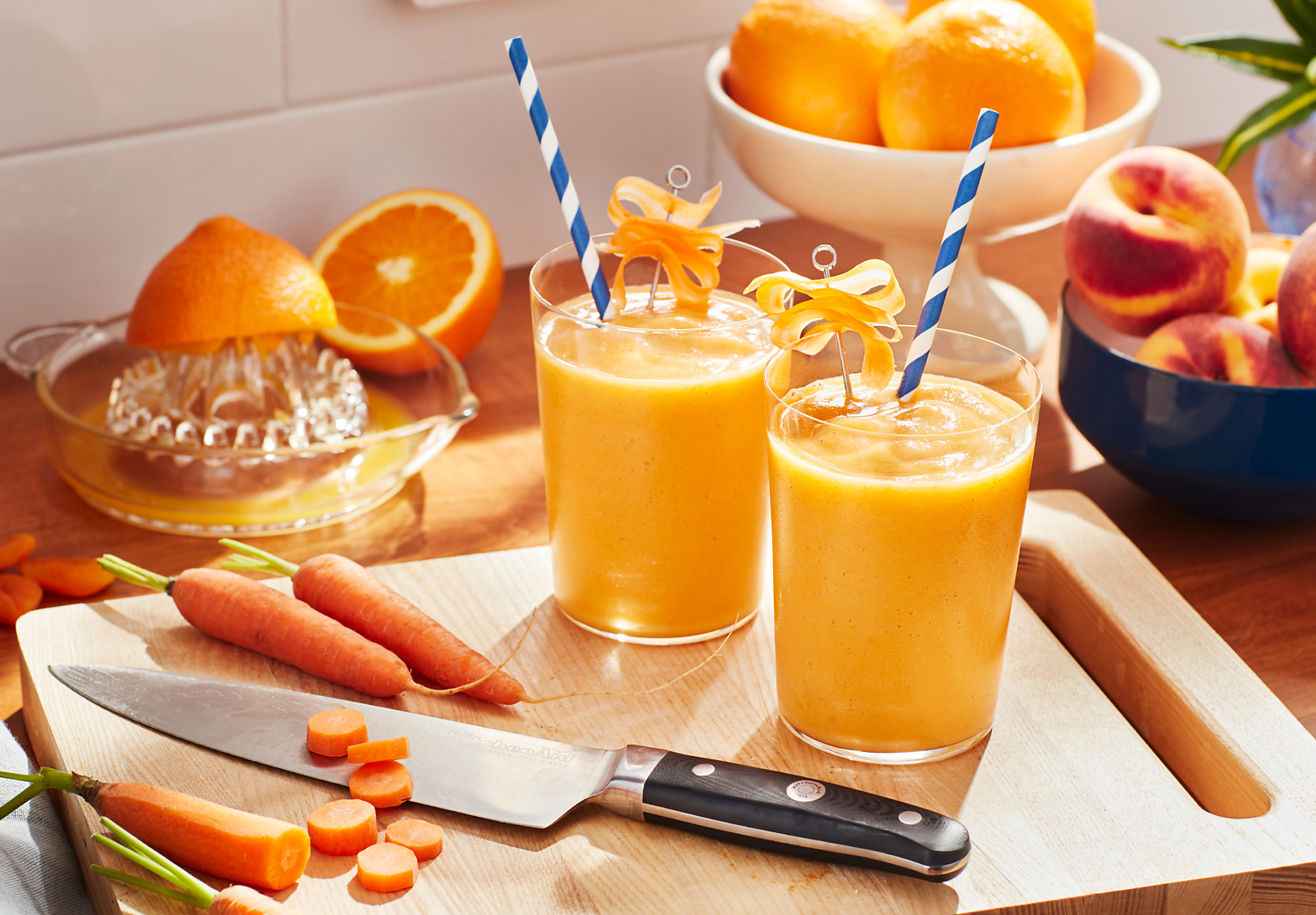 Glasses of orange juice with decorative straws on cutting board with carrots