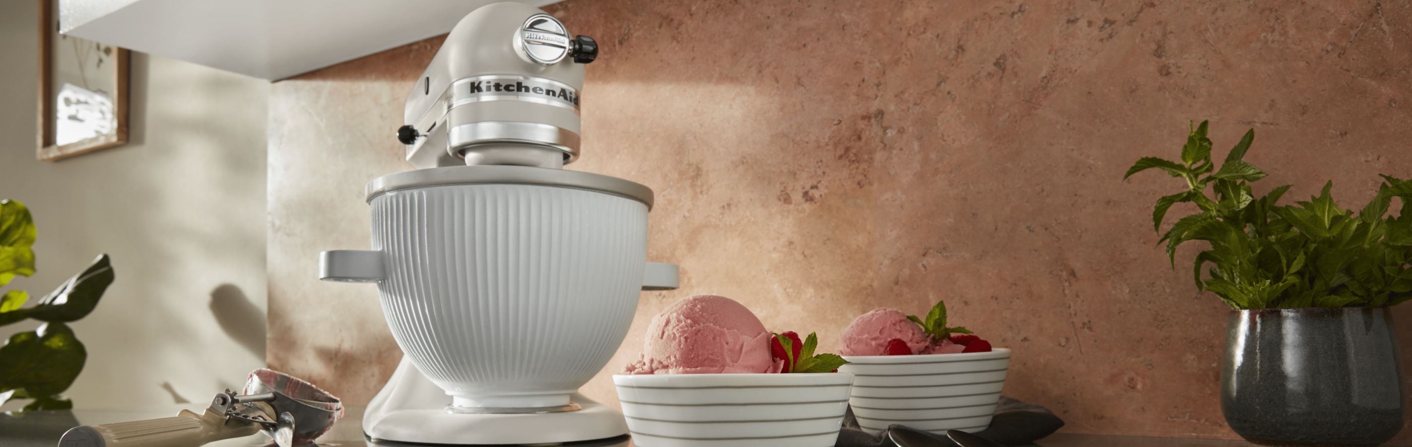 White KitchenAid® stand mixer with ice cream maker attachment next to bowls of strawberry ice cream