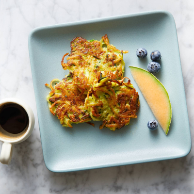 Zucchini herb fritters on a blue square plate with a cup of coffee