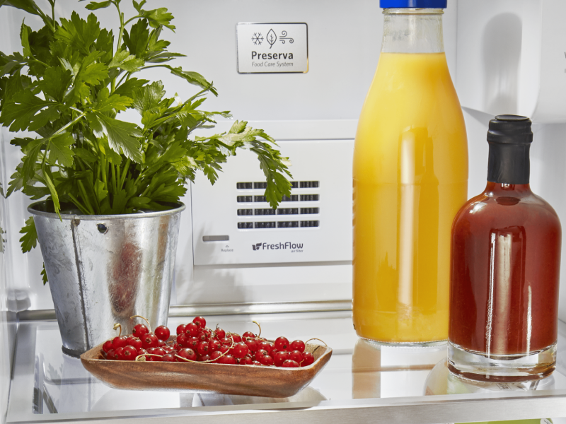 A jar of fresh orange juice and cherries on a refrigerator shelf.