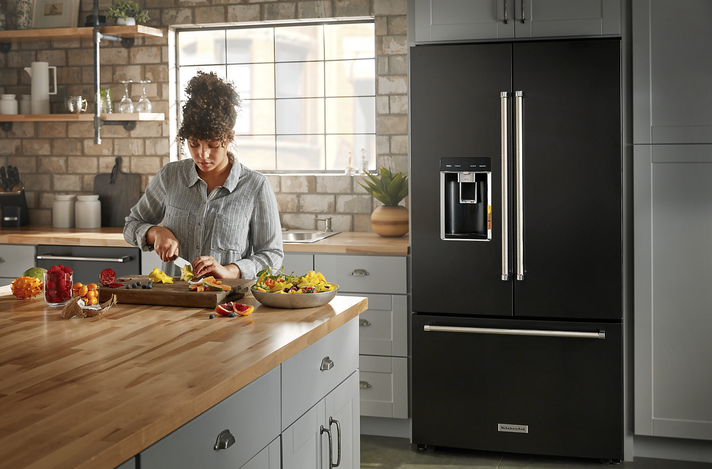 A person slicing fruit and a black KitchenAid® refrigerator.