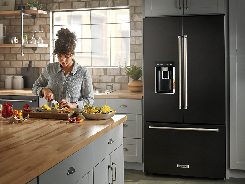 A person slicing fruit and a black KitchenAid® refrigerator.