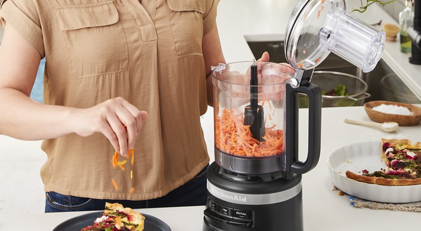 Person shredding carrots in a black food processor