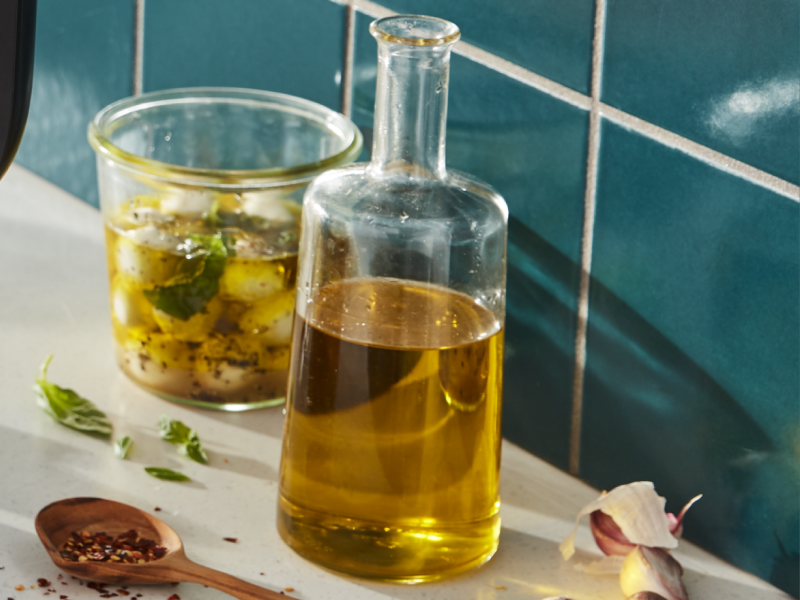 Bottle of olive oil next to a glass jar of marinated mozzarella 