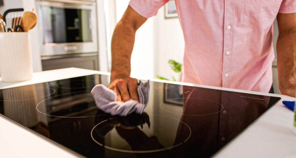 A person cleaning an induction cooktop.