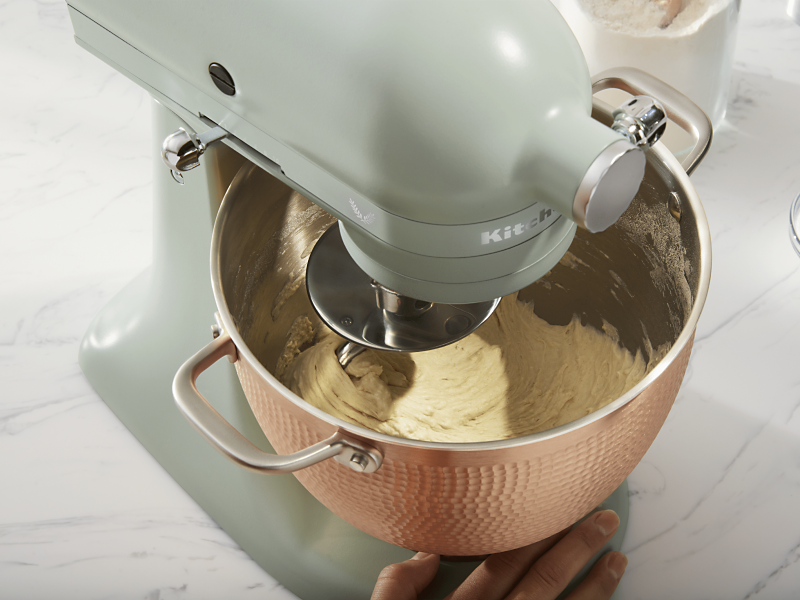 Person making pretzel dough in rose gold, textured stand mixer bowl