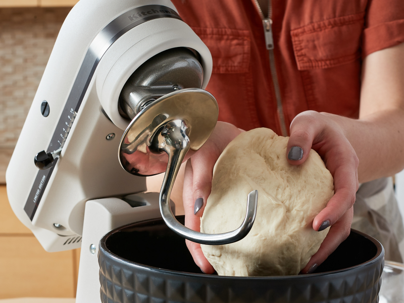 Person shaping ball of dough above black textured stand mixer bowl
