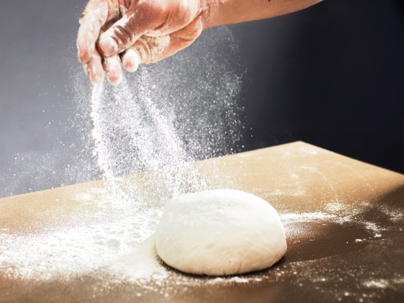 Person sprinkling flour on ball of dough sitting on a countertop