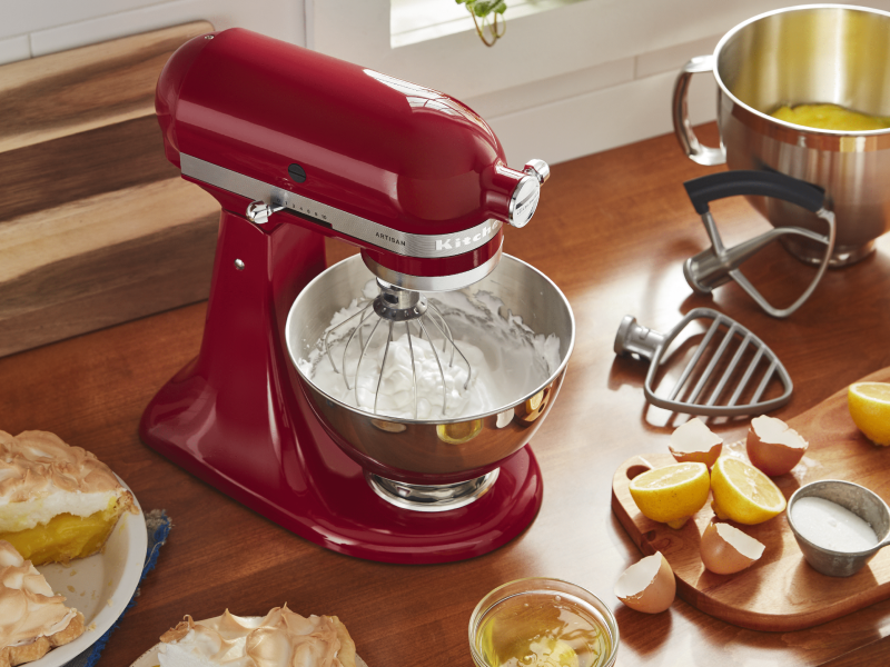 Red KitchenAid® Stand Mixer whipping meringue with lemon meringue pie, lemon curd and lemons on the counter next to the mixer 