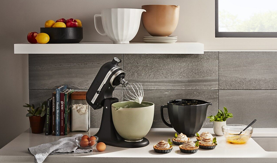 Black stand mixer on counter with various bowls and tartlette desserts Black stand mixer on counter with various bowls and tartlette desserts