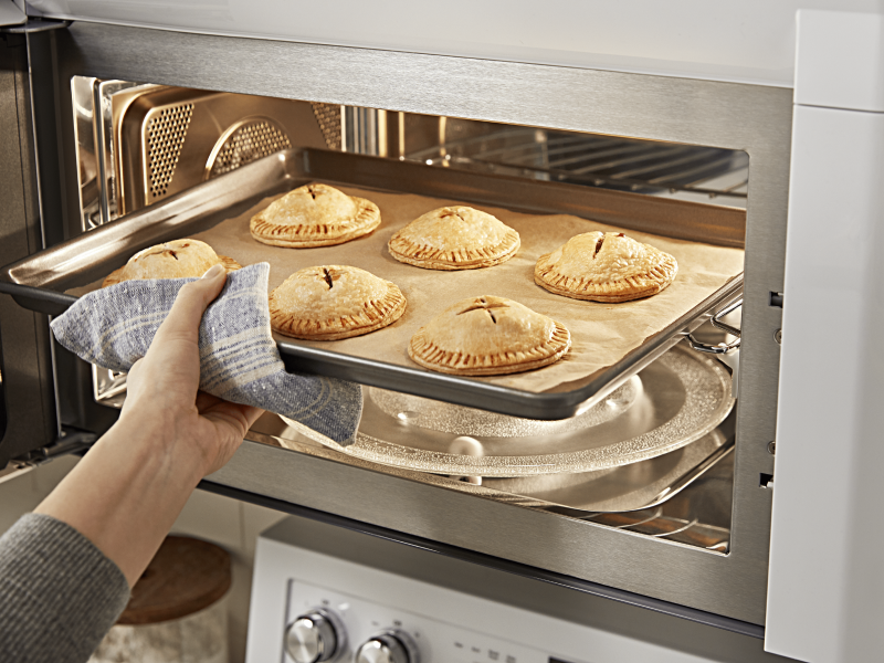 Person removing a tray of pastries from a convection microwave