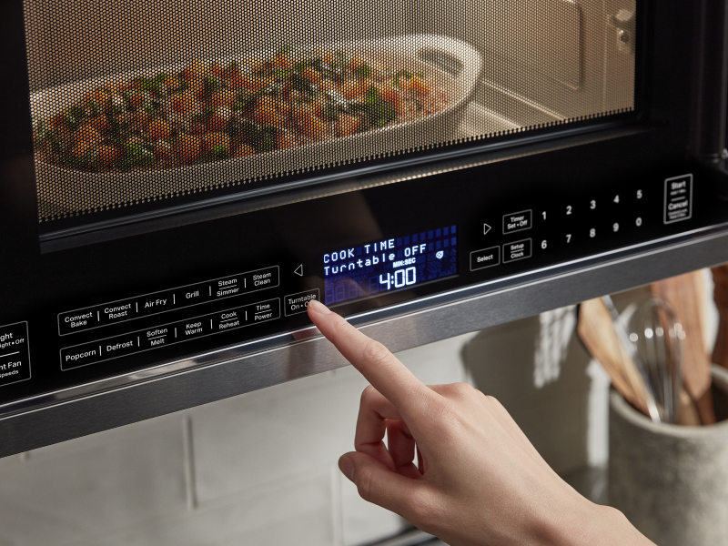 Person selecting settings on an over-the-range microwave steaming a vegetable medley