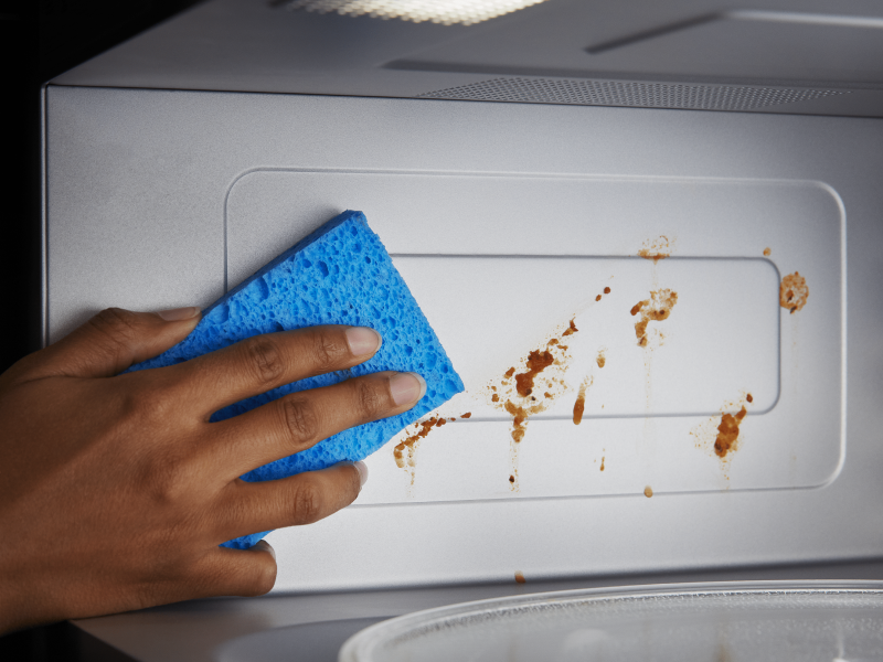 Person wiping down the inside of a microwave with a sponge