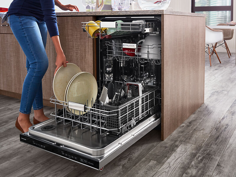 A woman placing a plate in a dishwasher