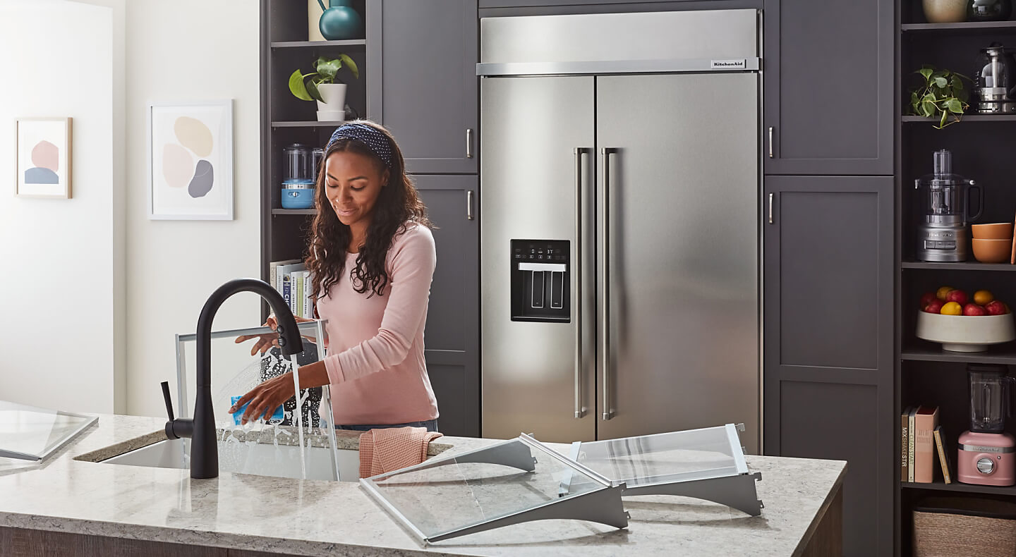Person washing dishes with KitchenAid® refrigerator in the background