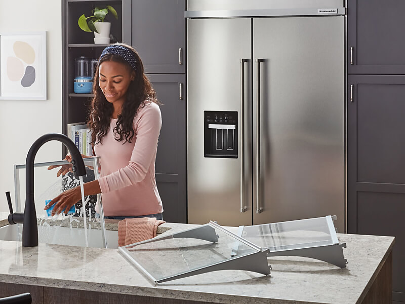 Person washing dishes with KitchenAid® refrigerator in the background