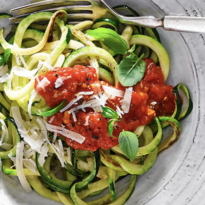 Zucchini noodles topped with grated cheese, red sauce and fresh herbs