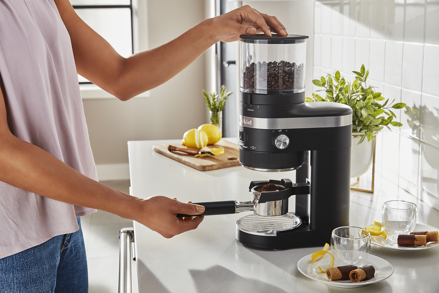A woman using a black KitchenAid® Burr Coffee Grinder to process coffee beans