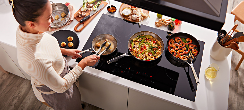 Person cooking pasta and shrimp on a black electric cooktop