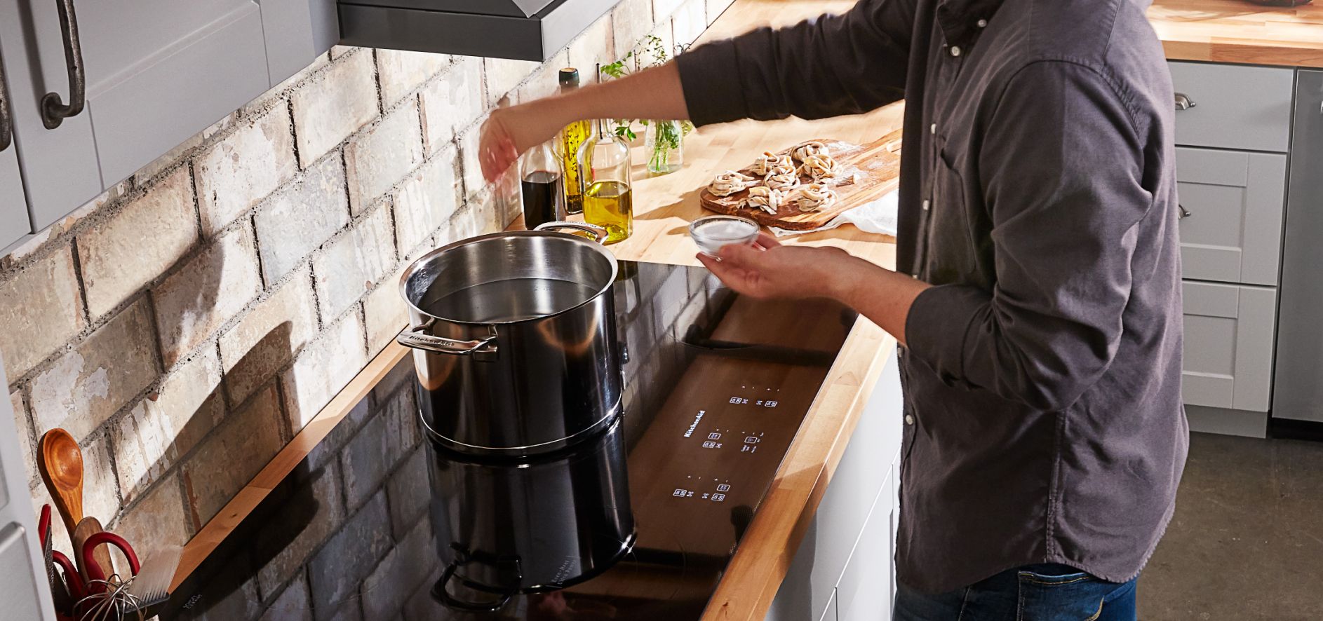 Person adding seasoning to a large pot on a black KitchenAid® cooktop