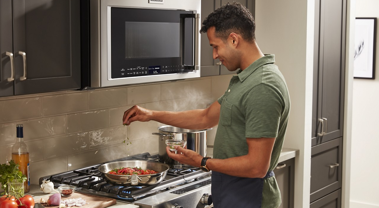Person putting seasoning on food in a pan cooking on a gas range