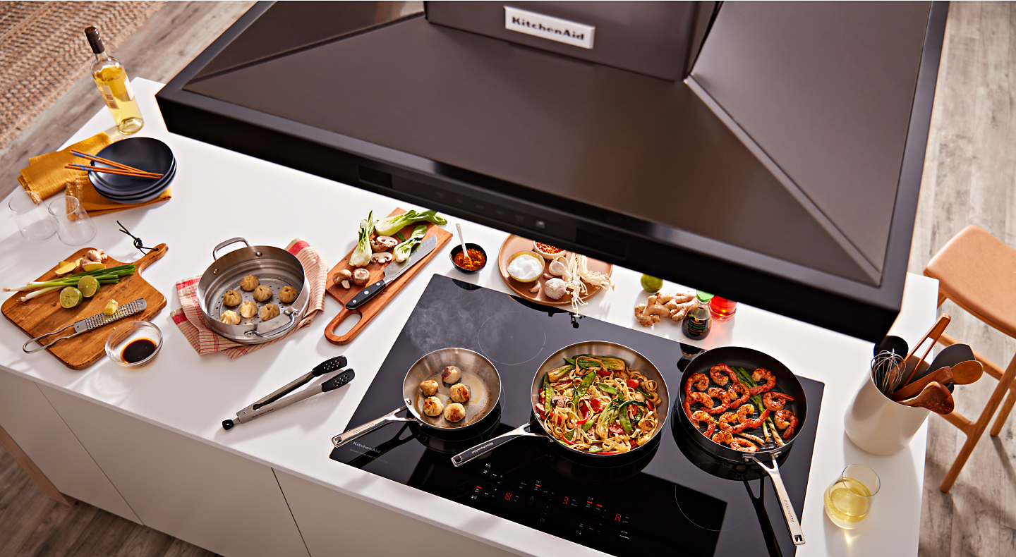 Overhead view of KitchenAid® range hood and pans with food on black cooktop
